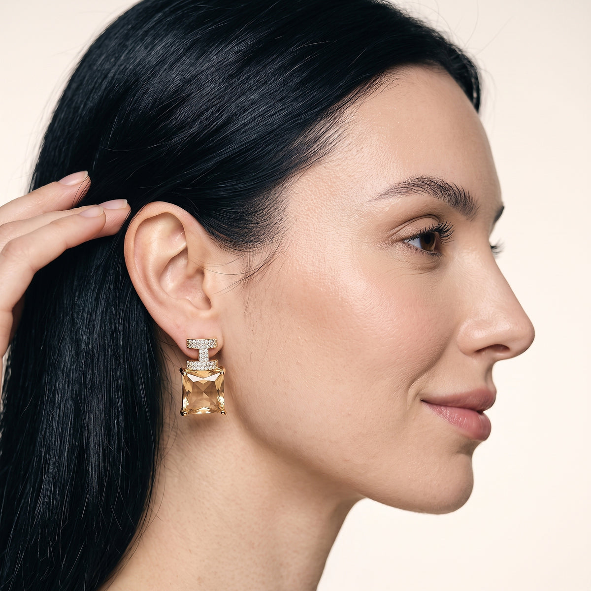 Modelo usando o brinco cravejado com pedra rosa banhado a ouro da ALUENA, de perfil com a mão no cabelo