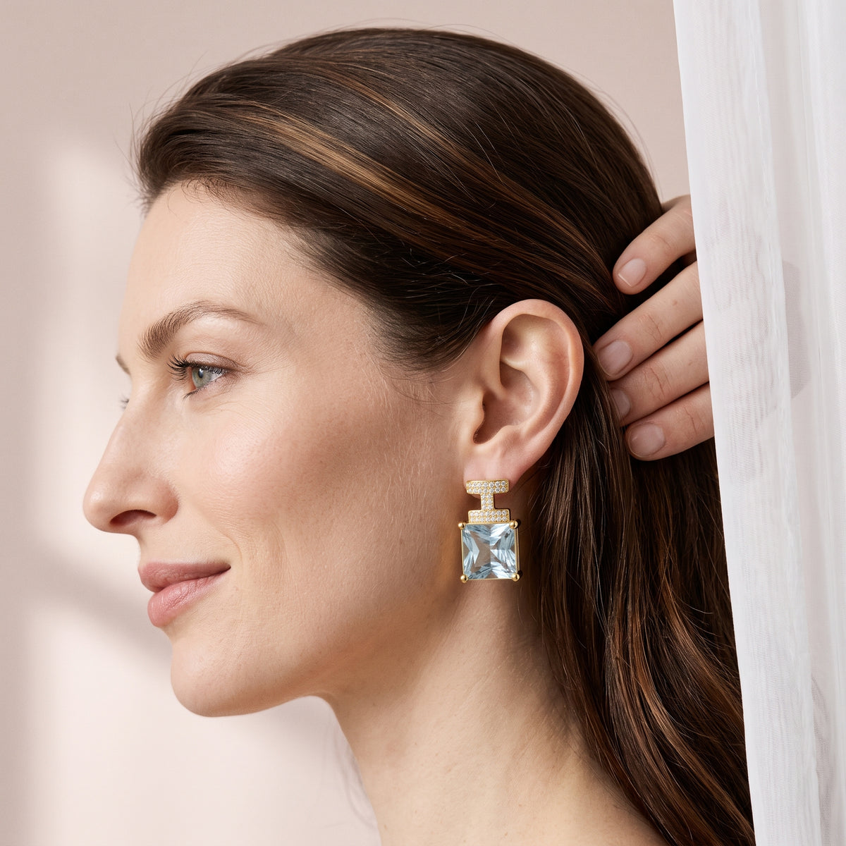 Modelo usando o brinco cravejado com pedra azul clara banhado a ouro da ALUENA, de perfil